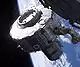 A module suspended in space by the ISS robotic arm. In view are the module's two compartments, the short, wide equipment lock to the left of the image, and the long, narrow crew lock to the left. The Earth and blackness of space are visible in the background, with the blurred corner of another module visible in the foreground, at top-right.